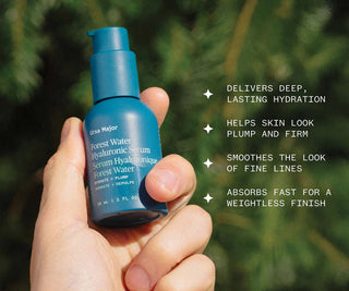 Blue serum bottle held in a hand with greenery in the background