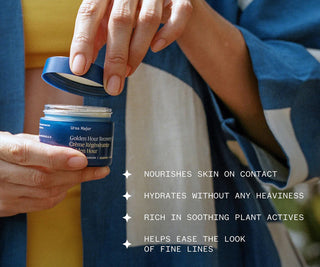 Person opening a jar of Ursa Major Golden Hour Recovery Cream with product details on a blurred background