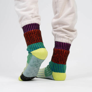 Colorful striped house socks worn with white pants on a light gray background