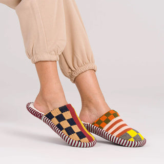 Multicolored checkered slippers worn with beige pants on a light background