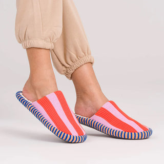Colorful striped slippers worn with beige pants on a light background