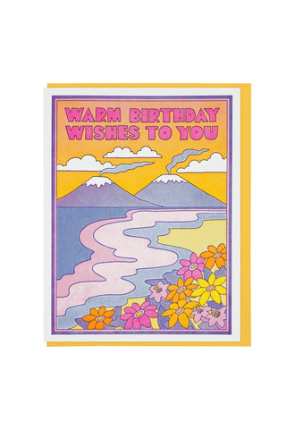 birthday greeting card with a colorful landscape illustration featuring mountains, a winding river, and flowers, with the text 'WARM BIRTHDAY WISHES TO YOU' 