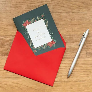 Red envelope with a green Christmas-themed card and pen on a wooden surface