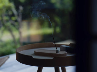 Incense stick with smoke on a wooden holder outdoors