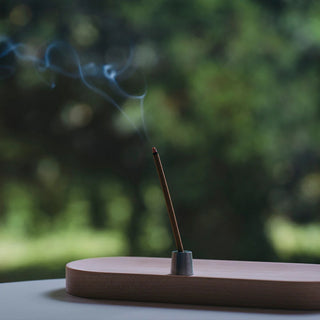 Incense stick with smoke on a wooden holder against a blurred green background