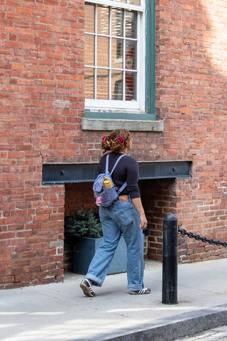 Person walking past a brick building with a backpack and colorful hair accessories.