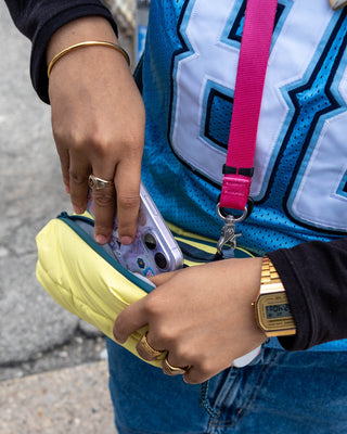 Person holding a phone in a yellow case with a blue jersey and pink lanyard in the background.
