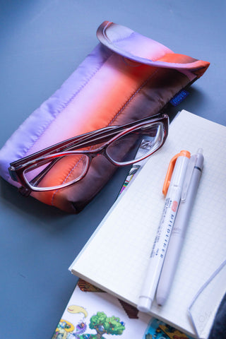 glasses on a pink case with a notebook and pens on a blue surface