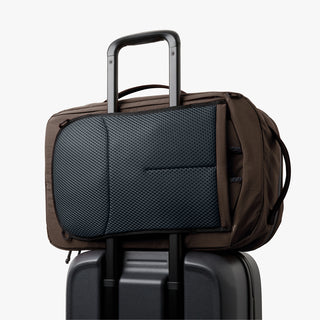 Brown travel bag with a black mesh pouch on top of a black suitcase