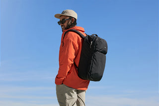 Person wearing an orange jacket and black backpack against a clear blue sky
