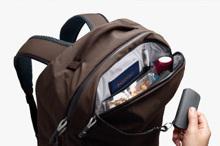 Brown backpack with items like a passport and a pen and hand holding keychain 