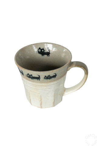 Overhead view of beige mug with cat parade design on a white background