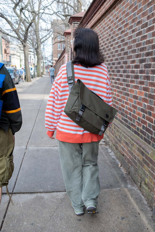 Person wearing a striped shirt and carrying a green bag on a sidewalk.