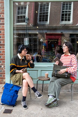 Two people sitting outside a store, one holding a coffee cup and the other a bag.