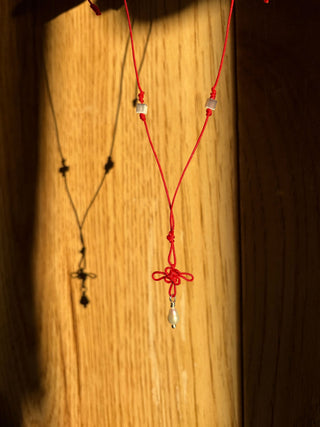 Red knot necklace with a small pearl with a wooden background