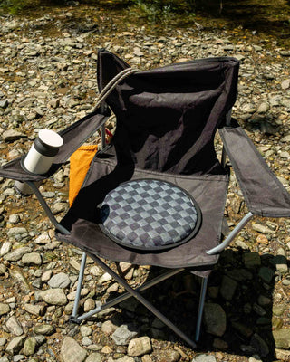 Peace Cabin ECLIPSE Seat Pad Checkerboard placed on a black outdoor folding chair set on rocky ground near a stream.