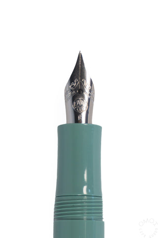 Close-up of a fountain pen nib and upper barrel in a sage green on a plain white background.