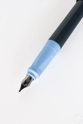 Close-up of a PERKEO fountain pen nib with a light blue grip and a black barrel on a white background.