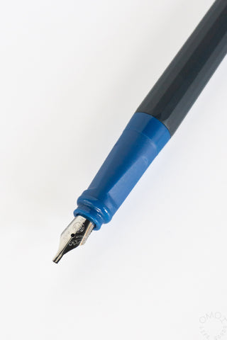 Close-up of a fountain pen nib with a dark blue grip, blue collar, and a dark gray barrel on a white background.