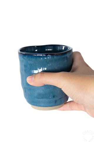 Hand holding a dark blue glazed ceramic teacup on a white background
