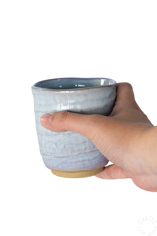 Hand holding a light blue glazed ceramic teacup on a white background