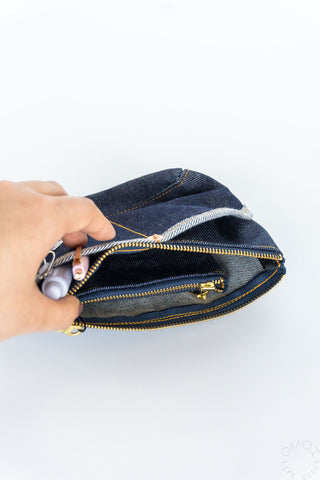 Hand opening a small denim Luddite pouch on a white background