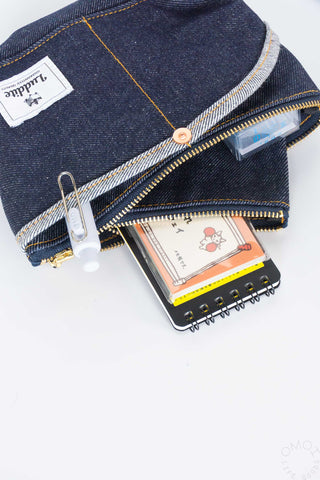 Close up of stationery inside a small denim Luddite pouch on a white background