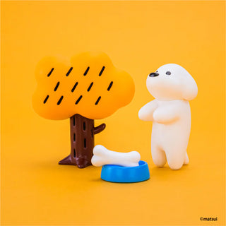 White dog figurine with a blue bowl and bone next to an orange tree on a yellow background