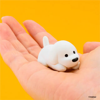Small white dog figurine held in a hand against a yellow background