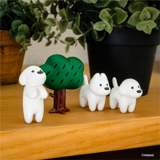 Three white dog figurines with a small green tree on a wooden surface.