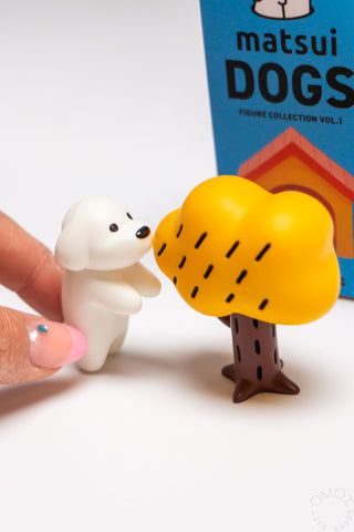 Small white dog figurine next to a yellow tree with a 'matsui DOGS' box in the background