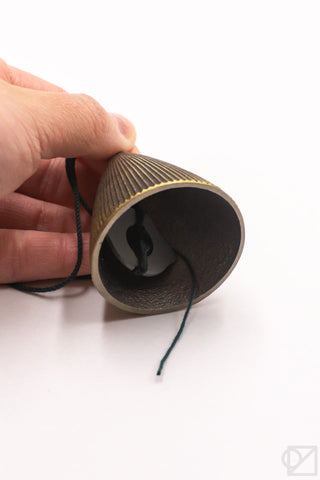 Hand holding a cylindrical wind chime with a string on a white background