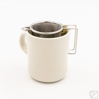 White ceramic mug with metal mesh tea infuser on a white background
