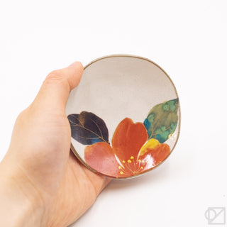 Hand holding a small ceramic dish with floral design on a white background