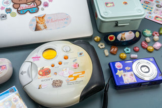 Vintage CD player with stickers on a blue surface surrounded by a laptop and camera
