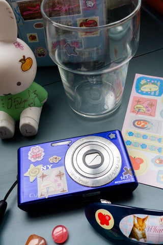 Blue camera and clear glass with nonalouie stickers on a blue background