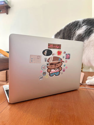 Laptop with stickers on a wooden desk, cat sitting behind