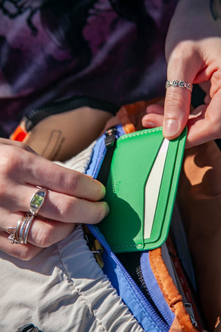 Close-up of hands with rings holding a green wallet against a blurred background