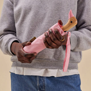 Person holding a pink umbrella with a wooden duck handle against a neutral background