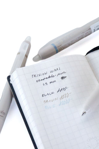 Erasable gel pen resting on grid notebook with written color notes