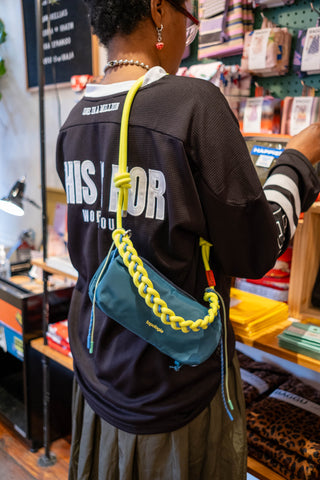 Person wearing a black jacket holding a blue bag with yellow strap in a store setting.