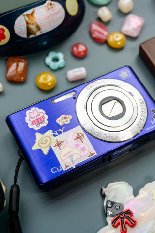 Blue camera with stickers on a blue surface with colorful beads