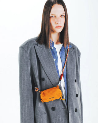 Person wearing a gray coat with a orange bag over their shoulder on a white background