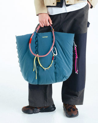 Person holding a blue tote bag with colorful handles on a white background