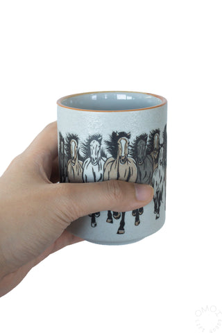 Horse teacup held in hand with black horse illustration on light blue body and orange rim